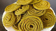 A plate of golden-brown keerai murukku, a type of Indian snack, displayed on a white plate.